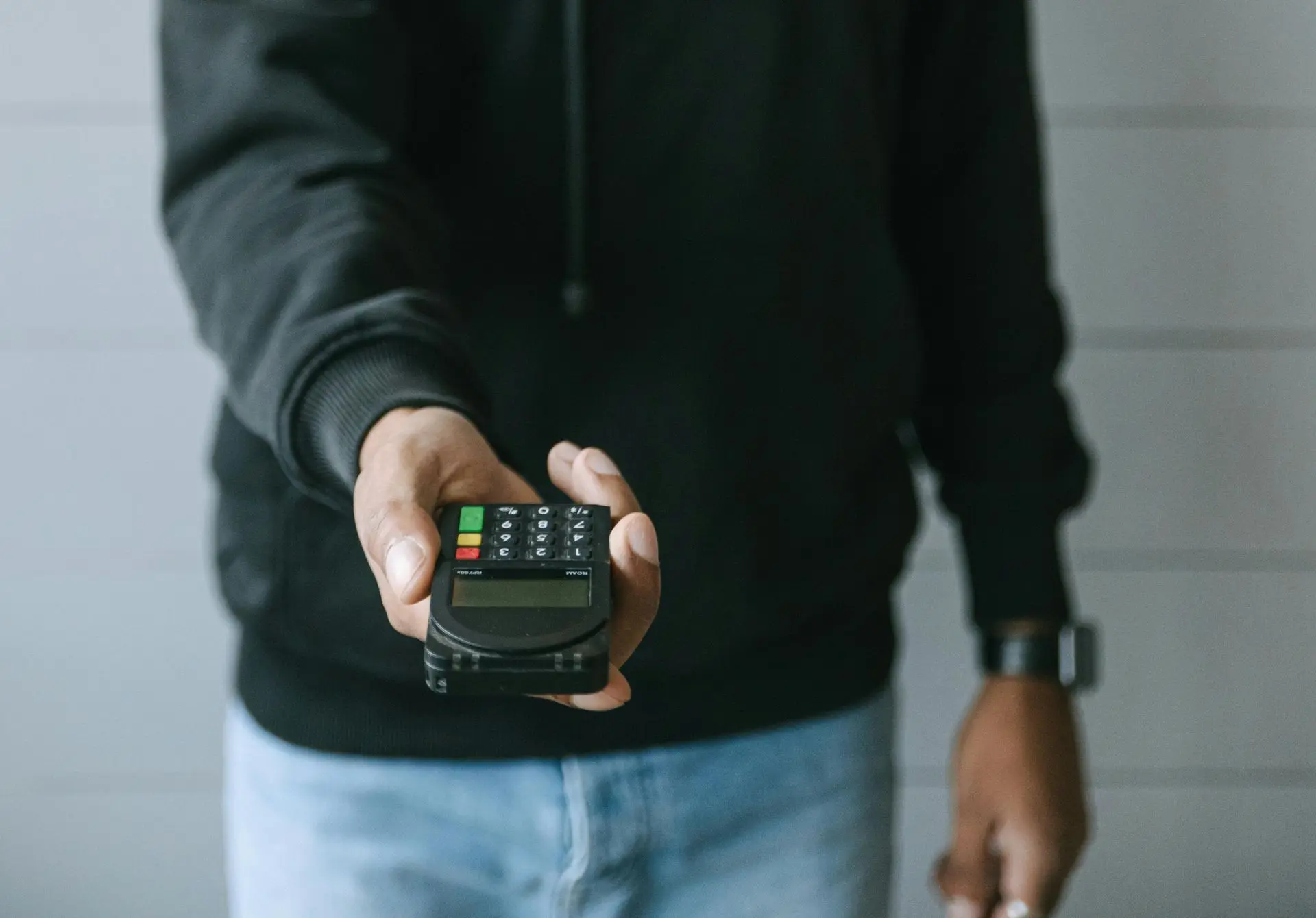 Individu en sweat-shirt tenant un terminal de paiement portable, illustrant la manipulation frauduleuse de la fonction crédit d'un TPE pour déclencher des remboursements non justifiés