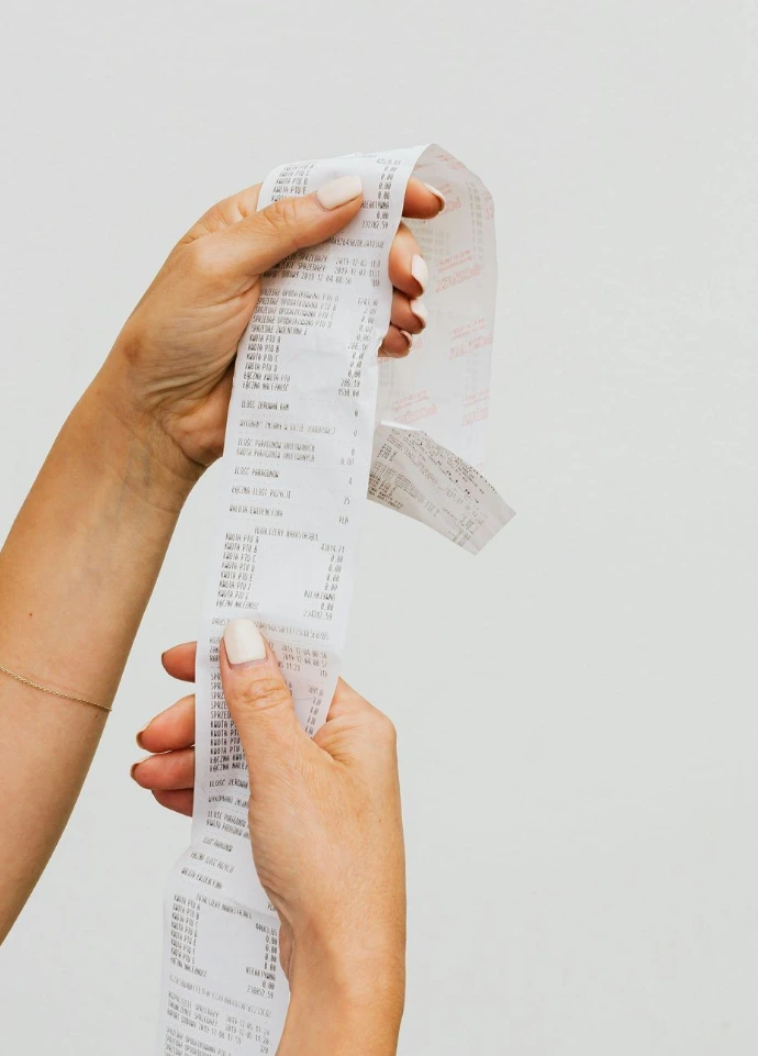 Mains tenant un très long ticket imprimé, symbolisant le ticket de télécollecte généré par un terminal de paiement (TPE).