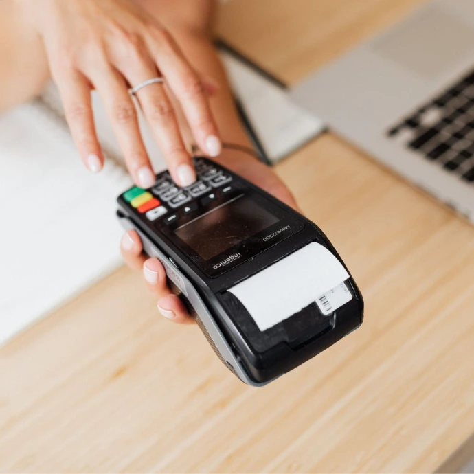 Mains d'un commerçant effectuant une opération de maintenance ou de vérification sur l'écran d'un terminal de paiement portable (TPE).